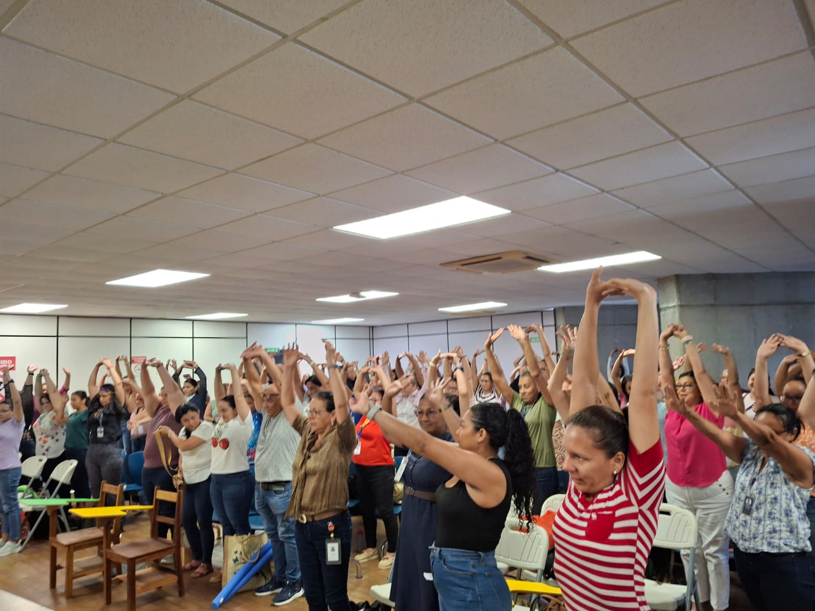 Participantes de pie con las manos extendidas hacia arriba realizando ejercicios de estiramiento